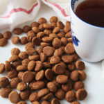 small brown cookies on a white backdrop next to a blue and white mug