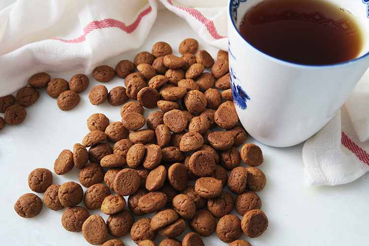 small brown cookies on a white backdrop next to a blue and white mug