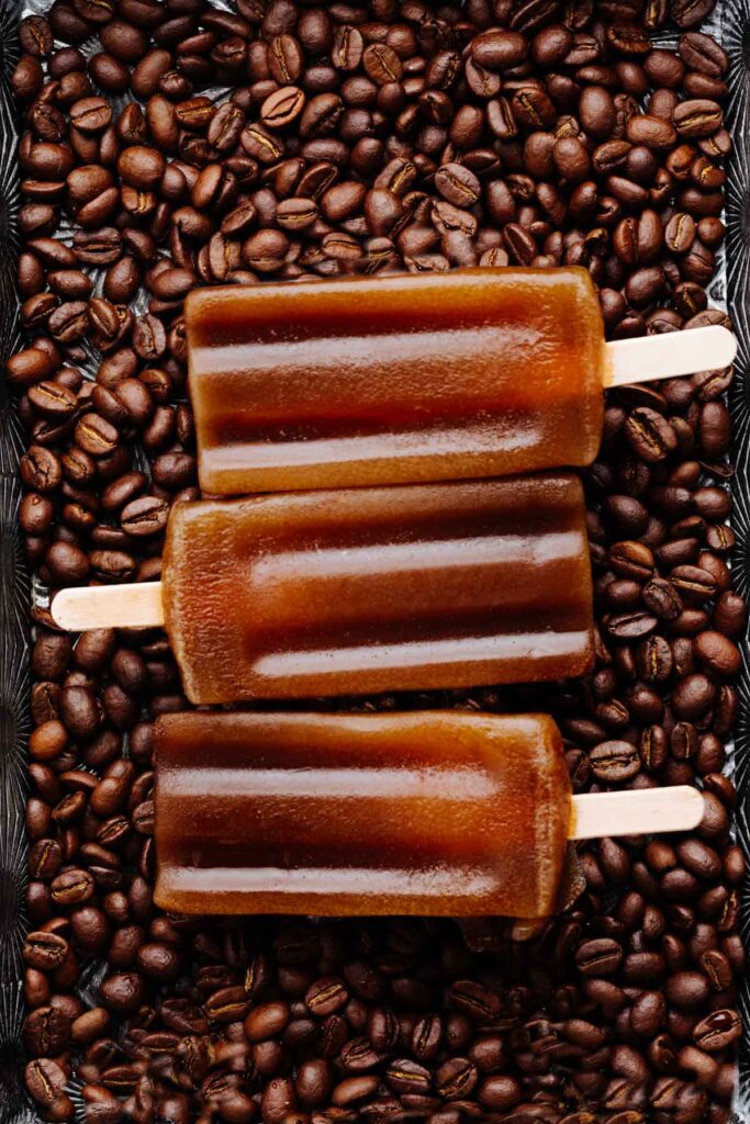 Close up of three brown coffee popsicles on a backdrop of coffee beans
