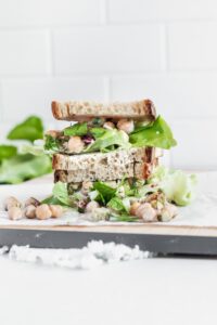 Chickpea Salad Sandwich with bread and lettuce sliced in half to show the inside on a wooden cutting board with a white backdrop