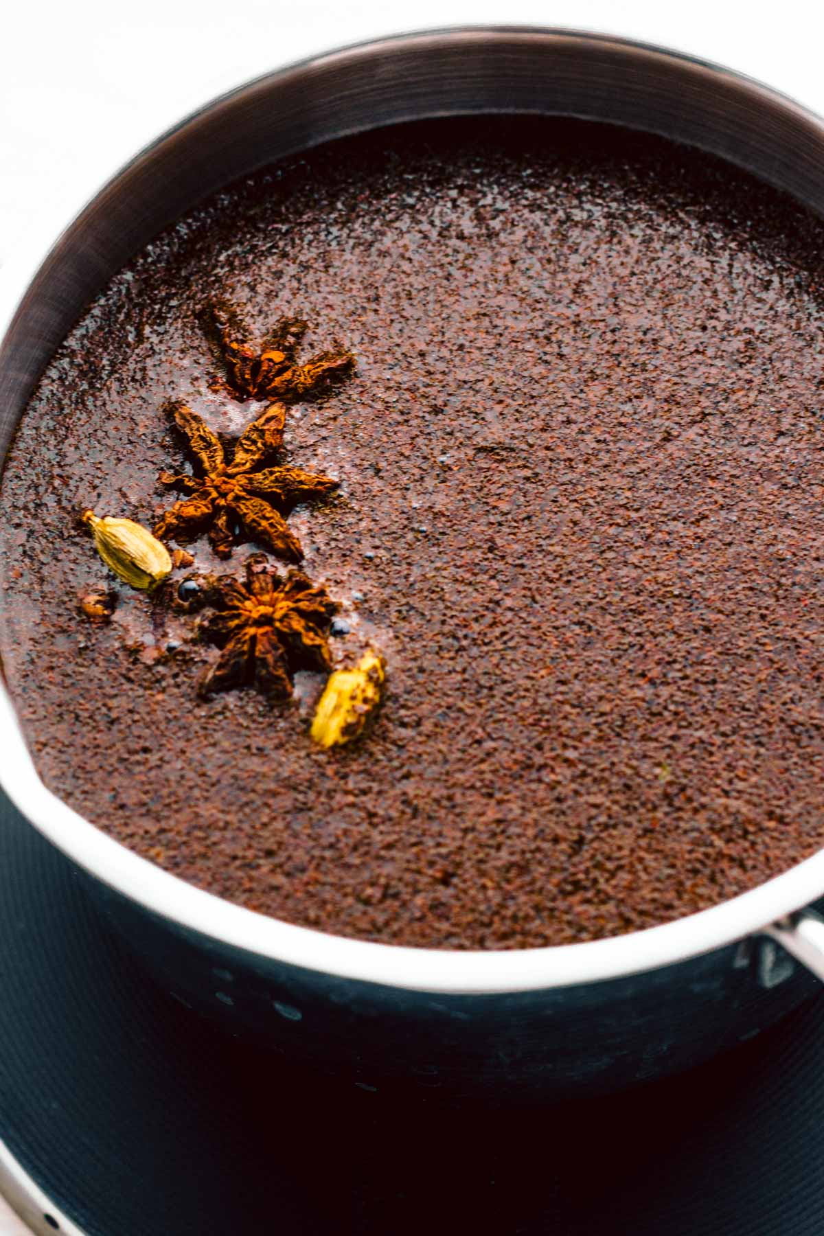 A stainless steel pan with dark brown tea showing black tea, star anise and cinnamon floating on top.