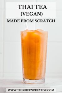 Bright orange colored Thai tea on a white marble cutting board in a tall glass with ice cubes and a glass straw with white tiles in the background with the title thai tea vegan made from scratch written on top.