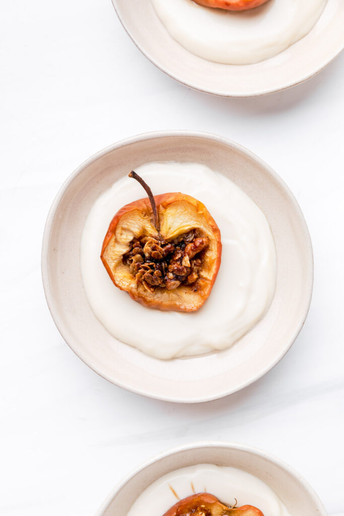 baked apple with filling in a beige bowl with soy yogurt on a white backdrop