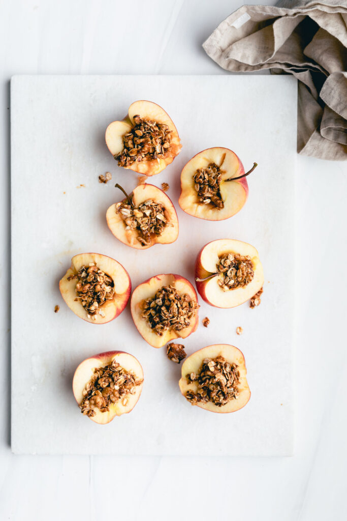 halved and cored apples filled with oat mixture on a white marble cutting board