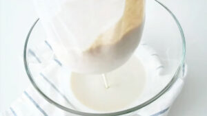 a filled nut milk bag is hanging above a glass bowl to be strained