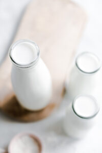 three bottles of plant-based milk on a wooden cutting board on a white backdrop