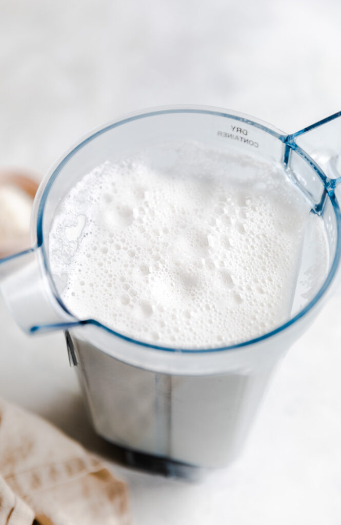 The top of a blender container with milk in it on a white backdrop