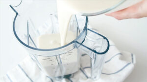 white plant-based milk being poured in the container of a blender