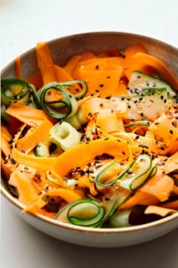 Cucumber and carrot salad sprinkled with white and black sesame seeds in a light brown bowl with a golden edge
