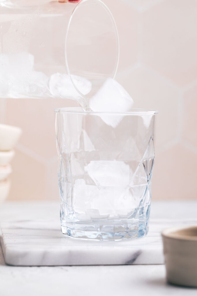A glass adding ice cubes to a serving glass.