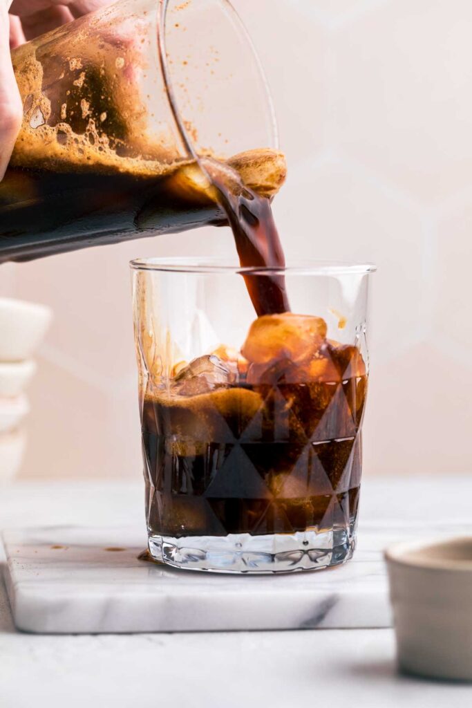 A glass with ice cubes with iced Brown Sugar Shaken Espresso being poured into it.
