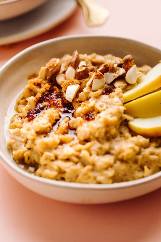 Close-up of Brown Sugar Cinnamon Oatmeal in a bowl topped with sliced apples, chopped almonds and melted brown sugar.