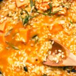 Creamy vegan pumpkin risotto in black cast iron pan with fresh rosemary and a wooden spoon