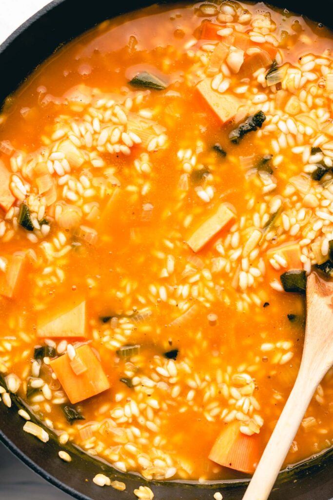 Creamy Arborio rice with sweet potato chunks and pumpkin broth in a black cast iron pan with a wooden spoon