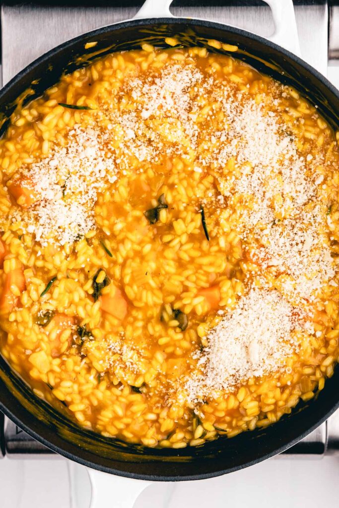 Creamy vegan pumpkin risotto in a black cast iron pan topped with vegan Parmesan cheese