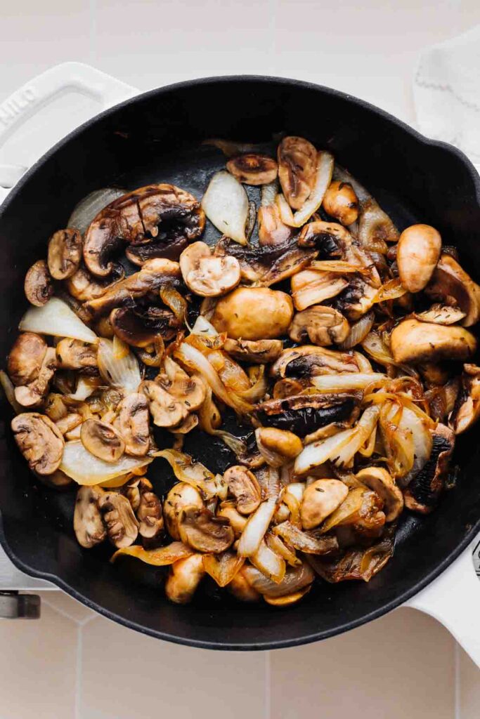 A black skillet with slightly caramelized sliced mushrooms and onions in it.