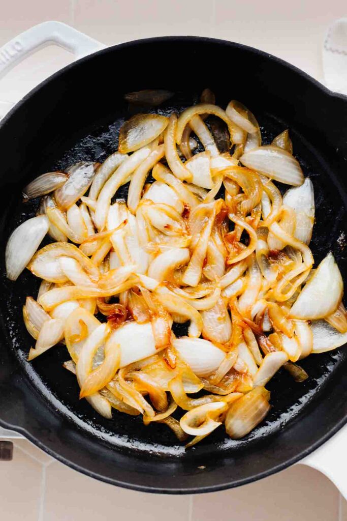 A black skillet with browned and glazed sliced white onion in it.
