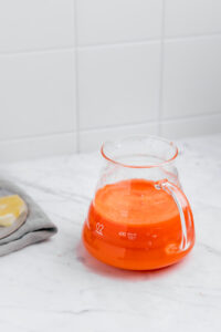 Carrot Ginger Turmeric Juice in a glass with a handle on a white marble table with a tiled white background