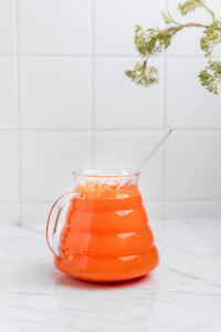 Carrot Ginger Turmeric Juice in a glass with a handle and a glass straw on a white marble table