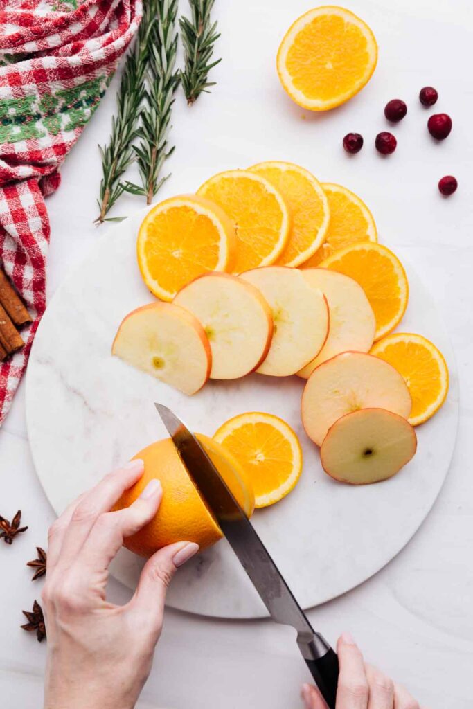 Sliced oranges and apples on a white marble backdrop.