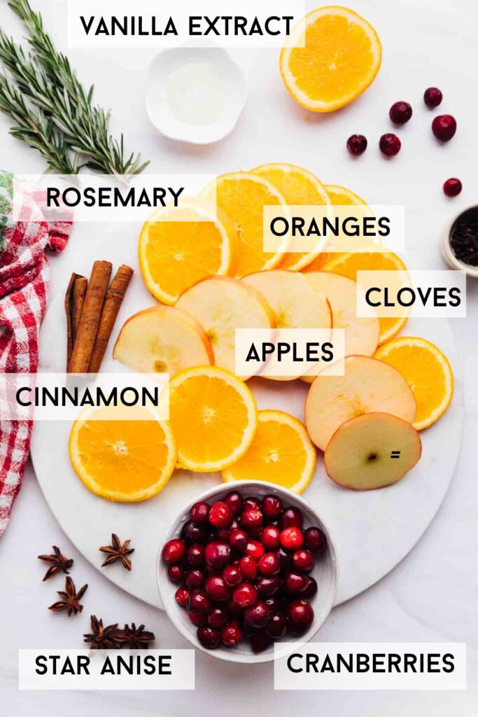 Ingredients for Christmas simmer pot on a white marble backdrop with descriptive labels.