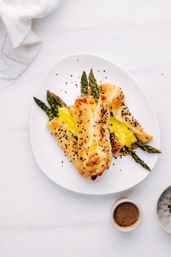 Three baked bundles with Asparagus with Puff Pastry on a white plate stacked on top of each other