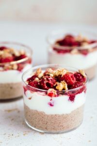 Three small glasses layered with brown pudding, then white yogurt and then red raspberries with chopped walnuts.