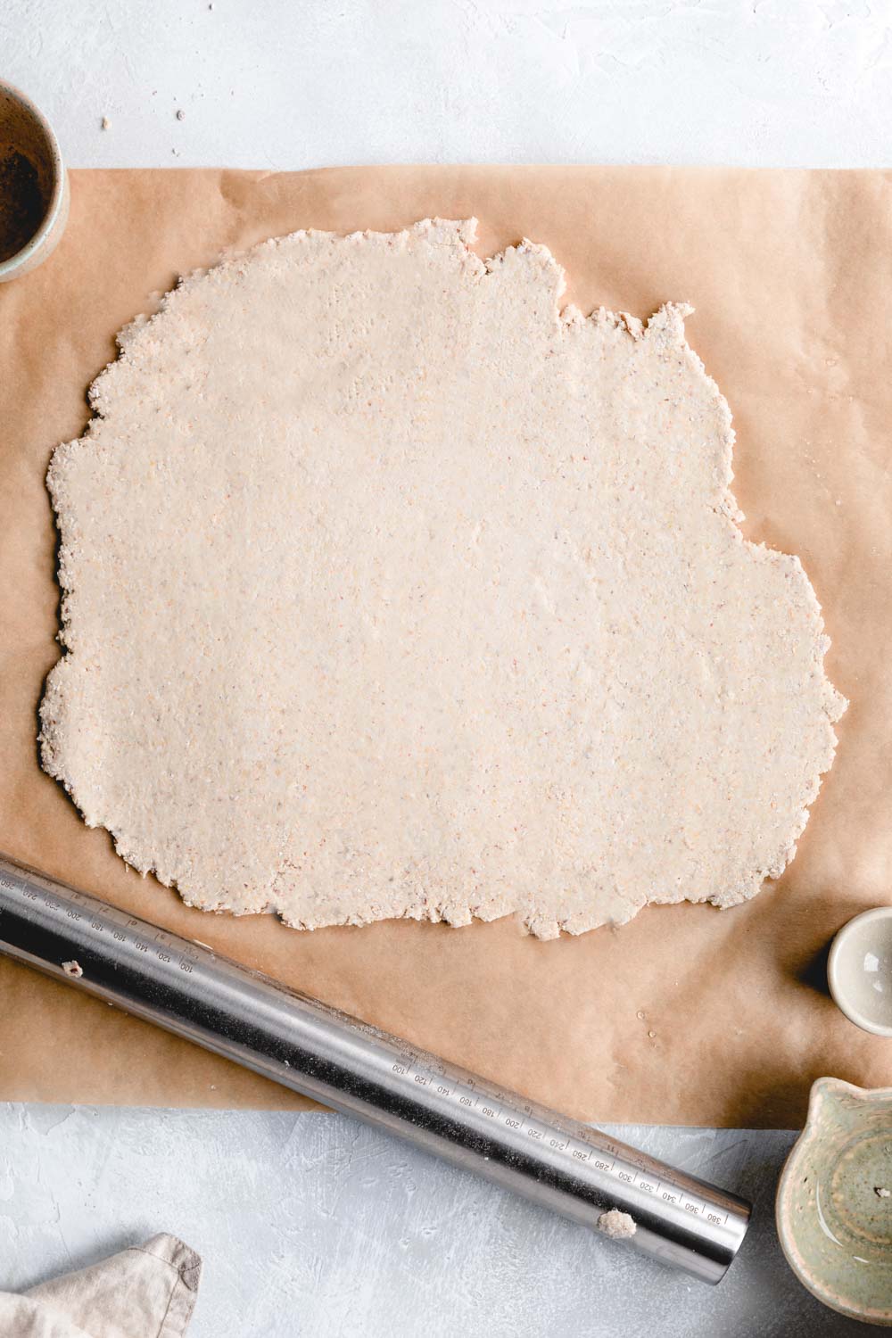 rolled out pie crust dough on brown parchment paper with a silver rolling pin next to it