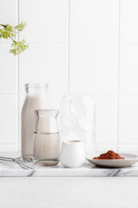 ingredients for iced chocolate on a white marble cutting board and a white tile backdrop