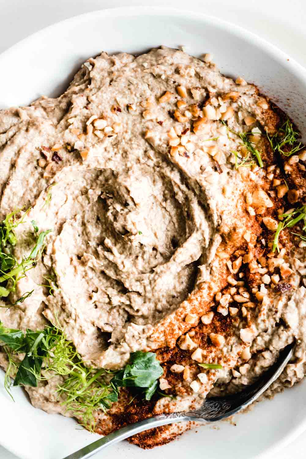 close up baba ganoush texture in a light bowl with fresh herbs, smoked paprika powder and chopped hazelnuts on top