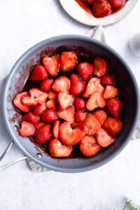 halved strawberries with juice and syrup in a blue pan on a light backdrop