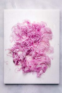 Thinly sliced red onions on a white marble cutting board.