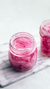 A glass jar with pickled red onions faced open on a marble cutting board