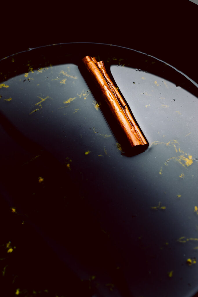 A close up of the inside of a black skillet with liquid in it and floating pieces of orange zest and a cinnamon stick.