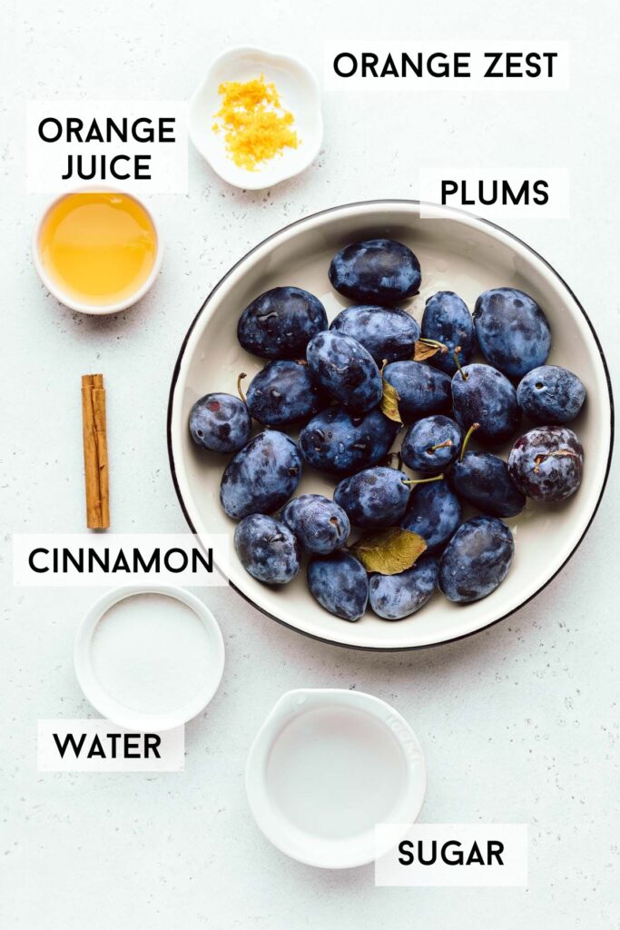 A light grey backdrop with a large bowl with blue plums in it and smaller bowls around it with orange juice, orange zest, water, white sugar and a cinnamon stick with the names of the ingredients written in bold next to it.