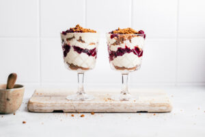 Two tall glasses with vegan parfait on a white wooden cutting board.