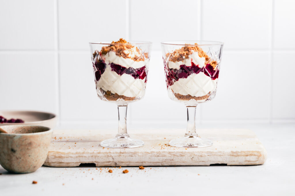 Two tall glasses with vegan parfait on a white wooden cutting board with small bowls next to it.