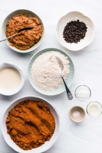 ingredients for vegan peanut butter chocolate chip cookies on a white backdrop in several bowls