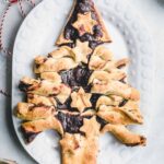 golden brown baked puff pastry christmas tree with stars on white oval plate on light grey backdrop