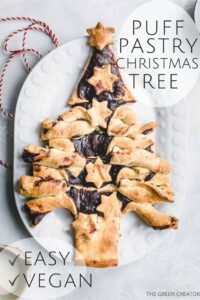 golden brown baked puff pastry christmas tree with stars on white oval plate on light grey backdrop