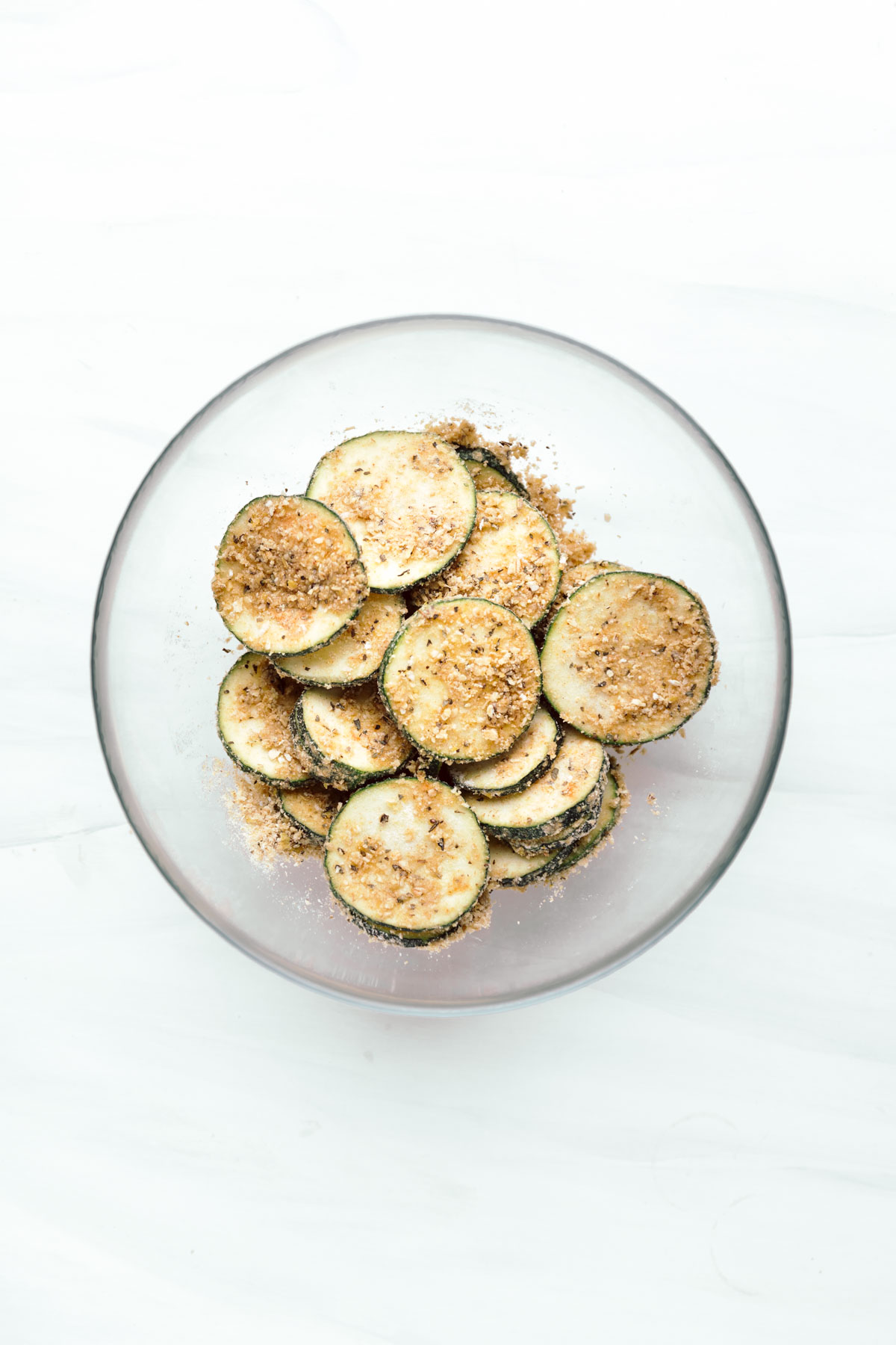 Brown coated zucchini slices in a glass bowl on a white backdrop