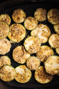 Brown coated zucchini slices in a black air fryer basket