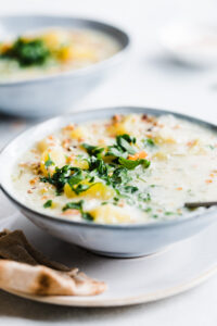 a side closeup of a bowl of cooked creamy potato soup with a piece of flatbread and parsley on top