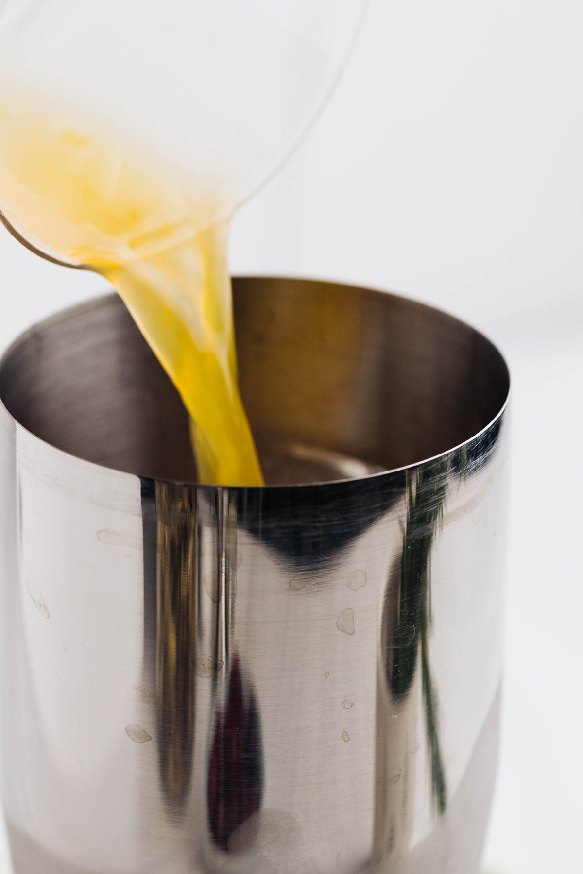 A silver colored cocktail shaker with a yellow liquid being poured in.