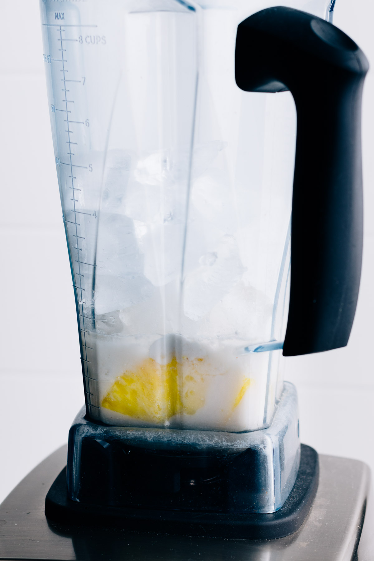 All ingredients for pina colada with ice cubes in a tall standing blender container