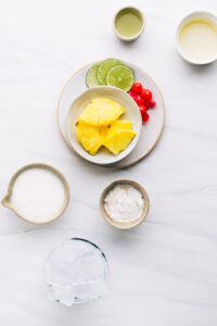 Ingredients for Piña Colada Mocktail on a white backdrop in several small bowls