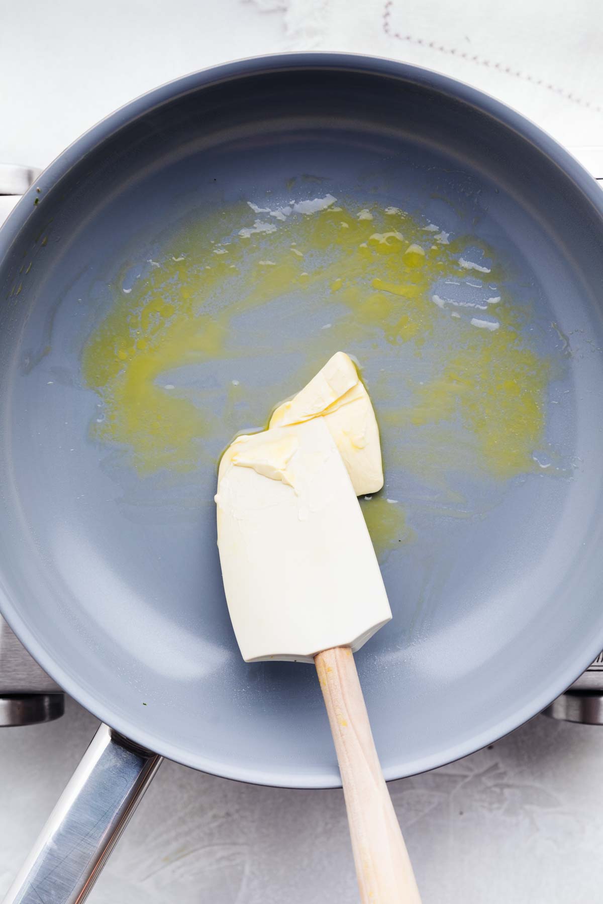 A blue pan on a little silver colored stove with melting butter in the hot pan and a spatula.