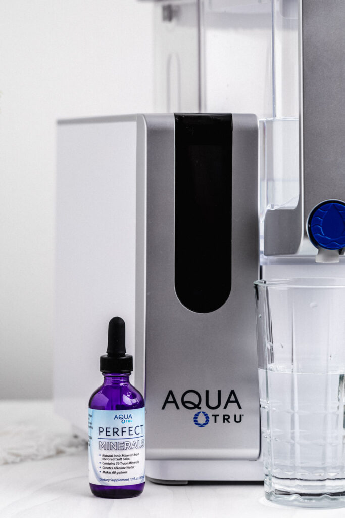 AquaTru water filter with a glass of water and a blue glass bottle of AquaTru minerals
