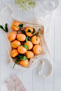 an open cotton shopping bag with mandarins and green leaves on a marble table