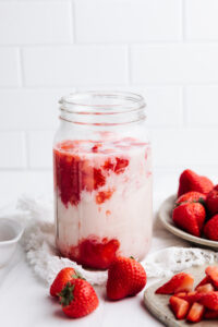 A large glass jar with a mixture of strawberries and milk on a white backdrop
